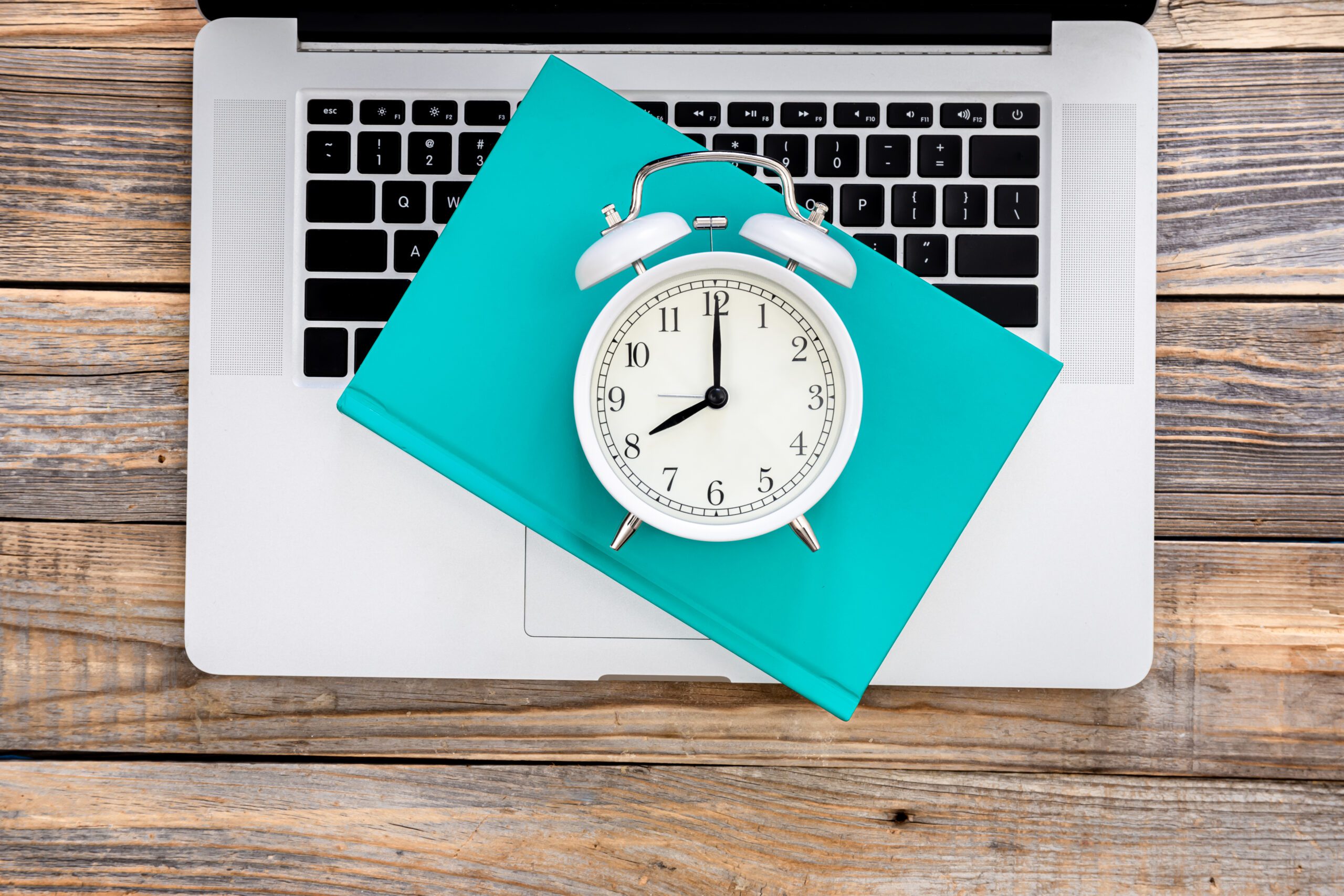 Best Day and Time to Send Emails: What Actually Works 1 Laptop, book and white alarm clock on wooden background, top view.
